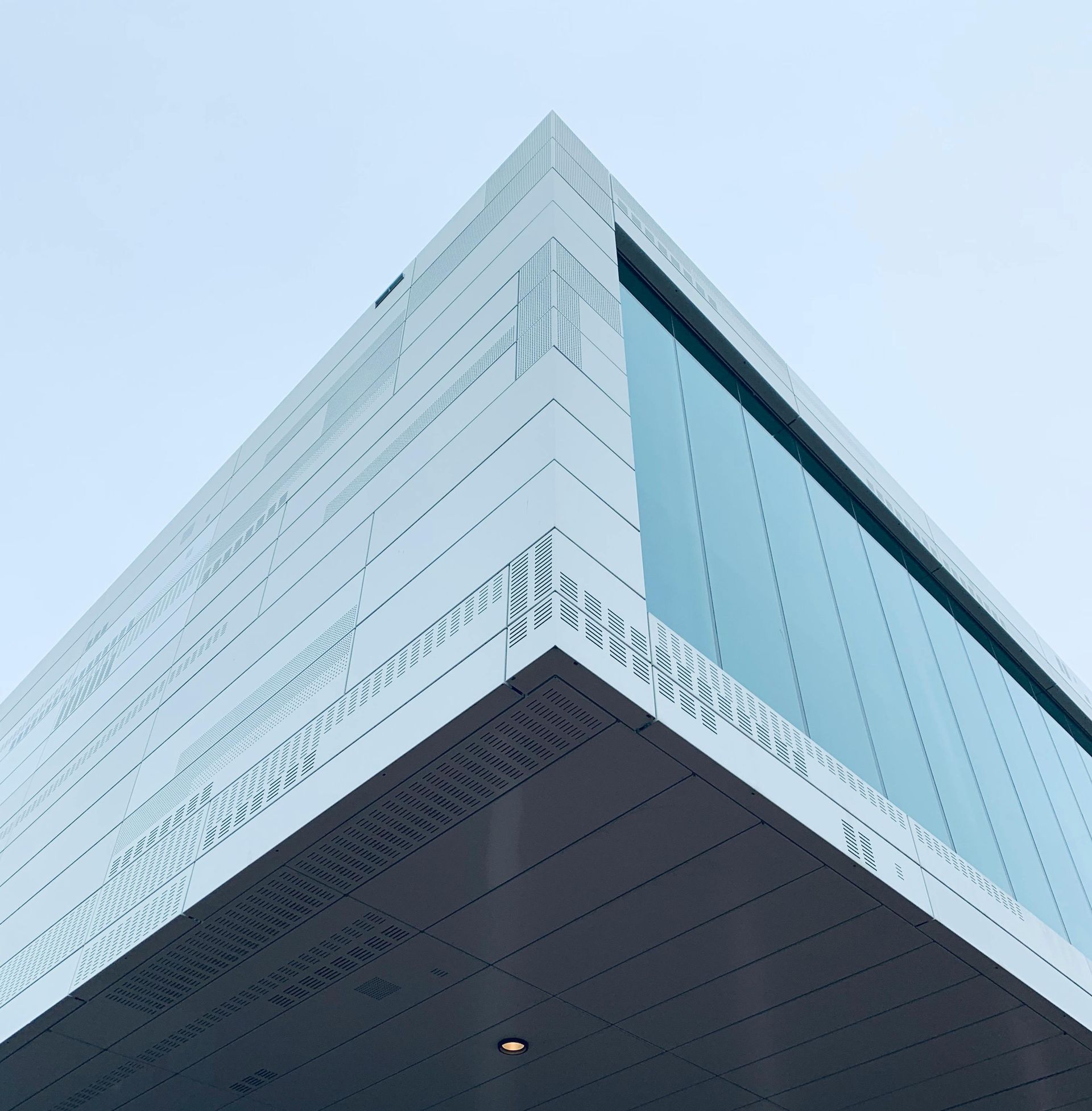 Modern white building corner with glass window, against a pale blue sky.