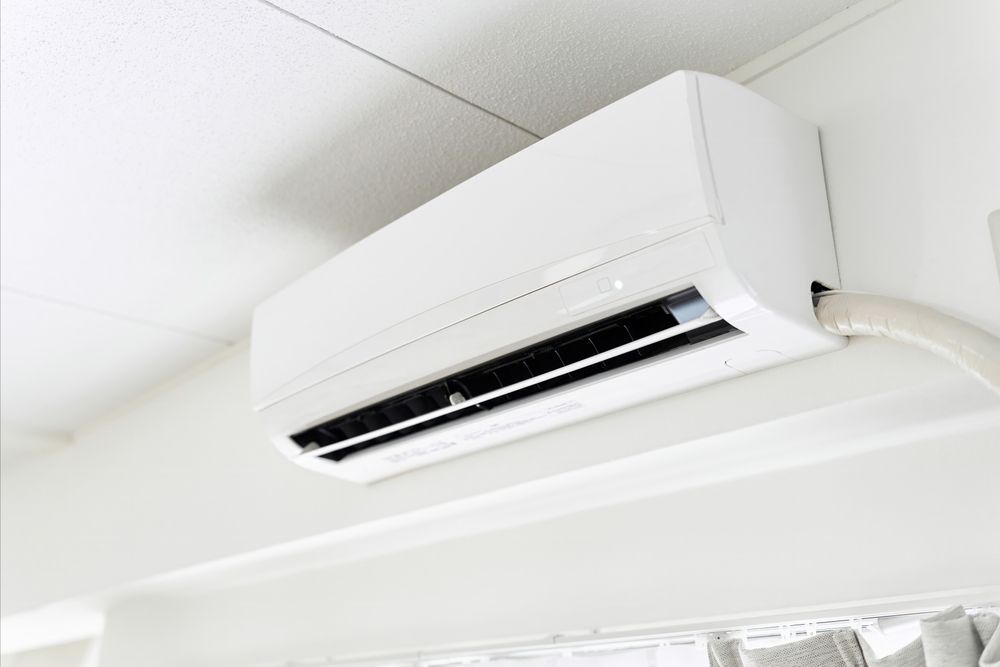 White wall-mounted air conditioner unit indoors against a white wall and ceiling.
