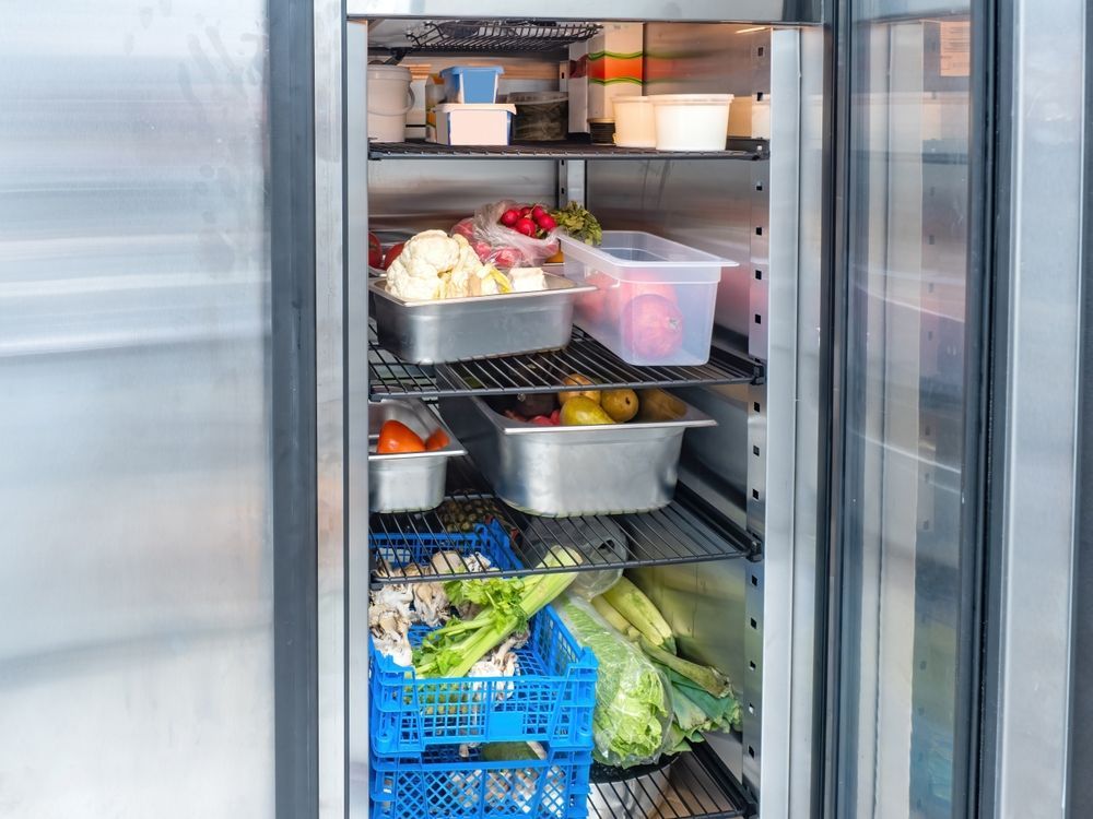 Open stainless steel refrigerator filled with food containers and produce.