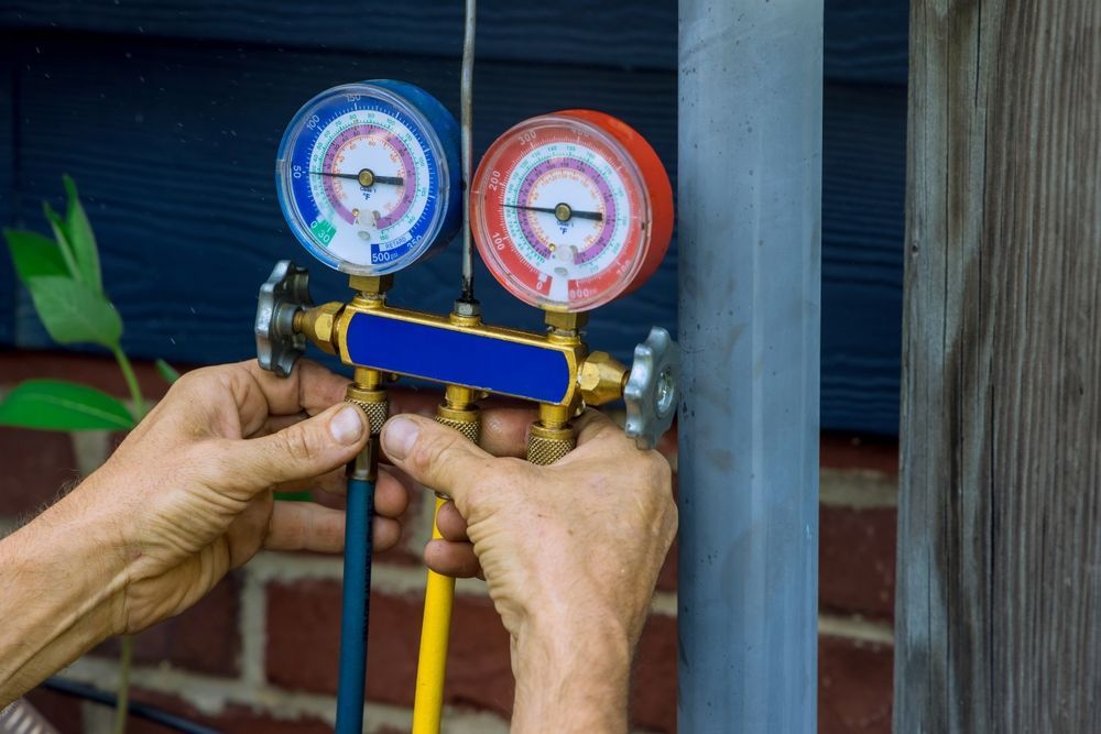 Hands connecting gauges to an HVAC system, blue and red pressure dials, outside near a wall.