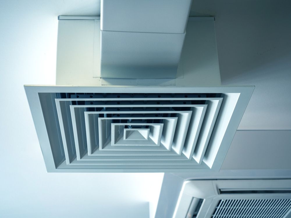 Ceiling-mounted air vent, square design, with layered slats. White, geometric, in a modern setting.