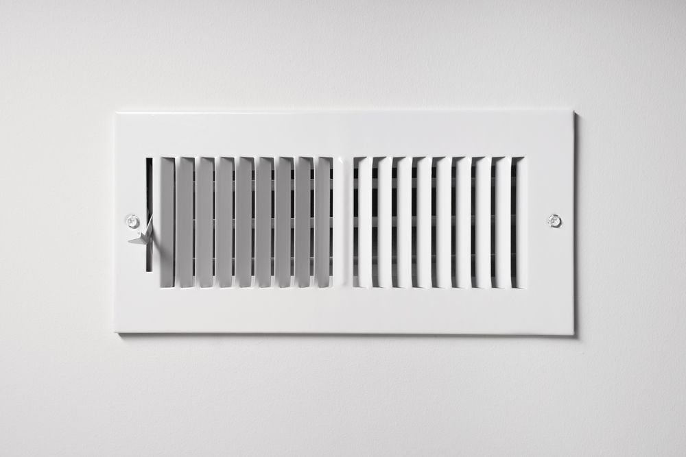 White air vent with adjustable slats on a white wall.