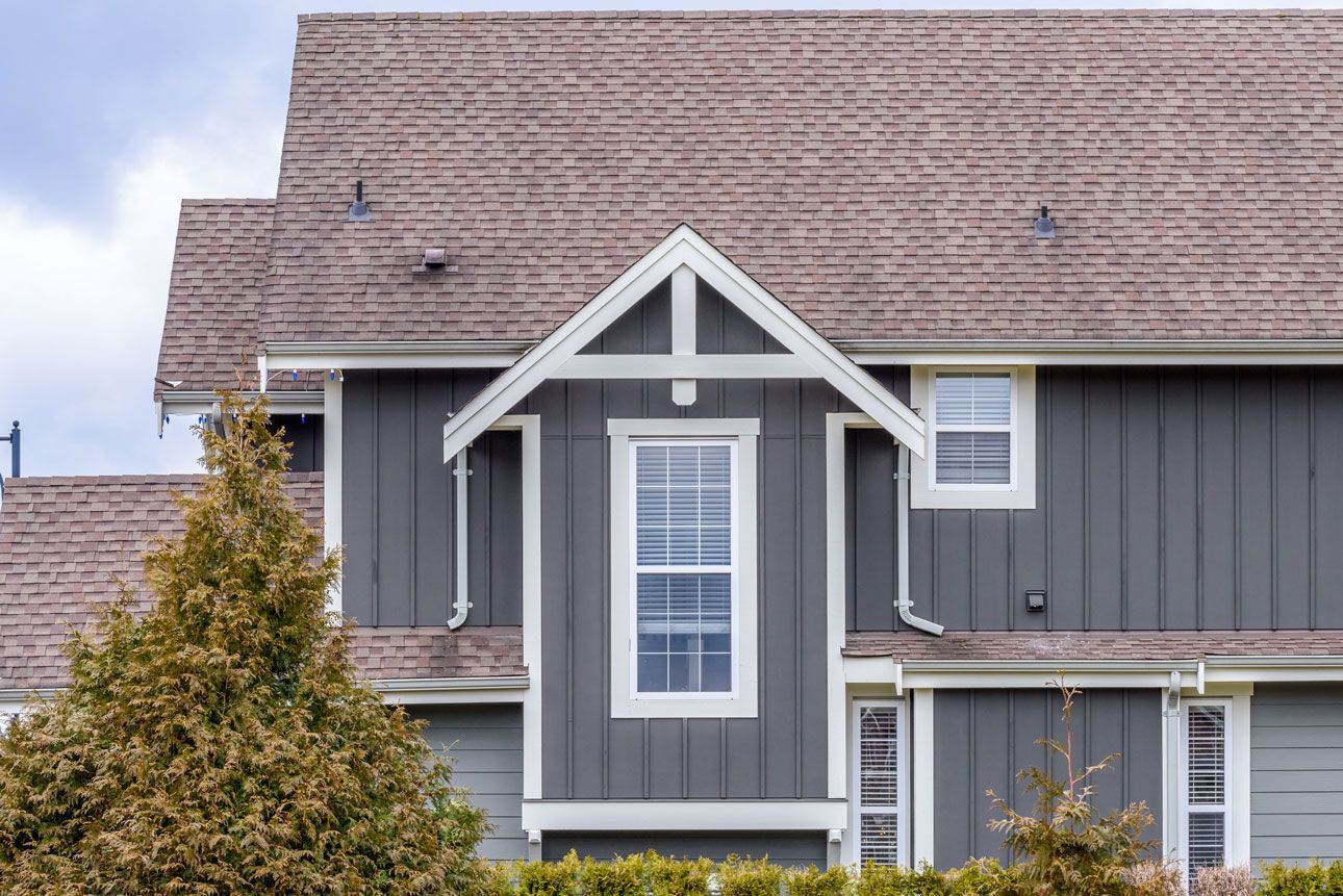 A gray house with a brown roof and a tree in front of it