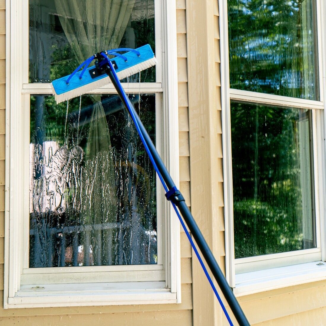 A window cleaner is cleaning a window with a broom.