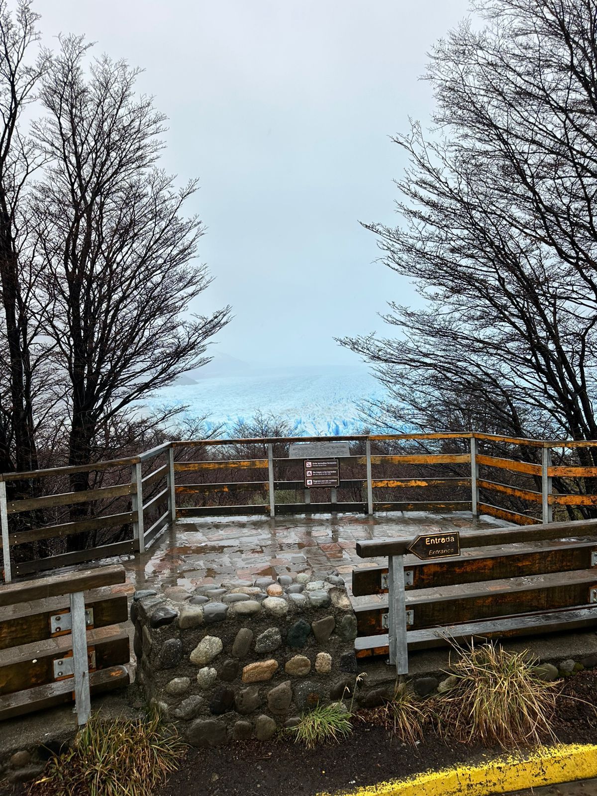 Una valla de madera rodea una plataforma de piedra con árboles al fondo.