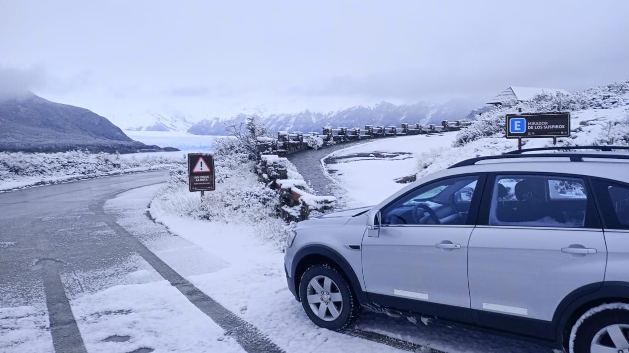 Un coche blanco está aparcado al costado de una carretera nevada.