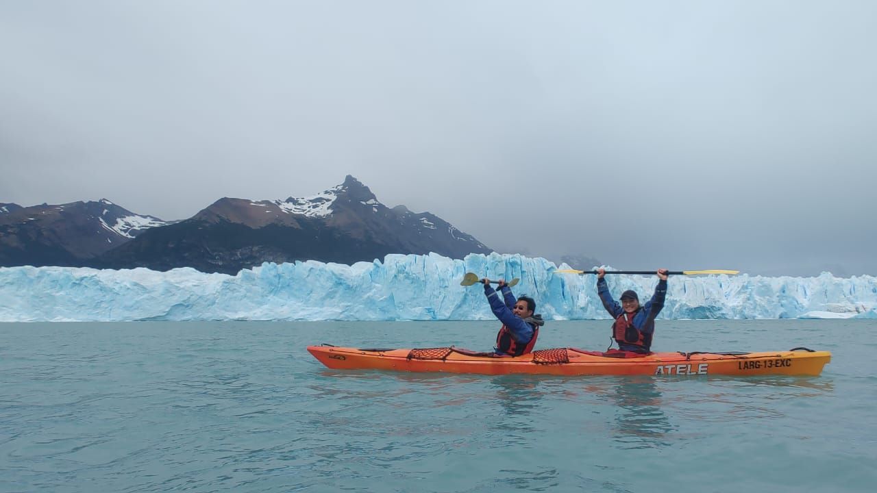 Dos personas están en un kayak en el agua con montañas al fondo.