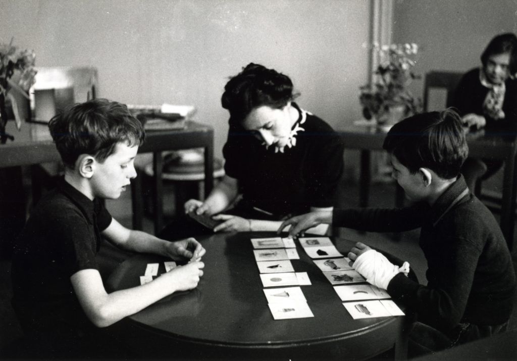A woman and two boys sit at a table, engaging with picture cards. The setting is calm and focused.