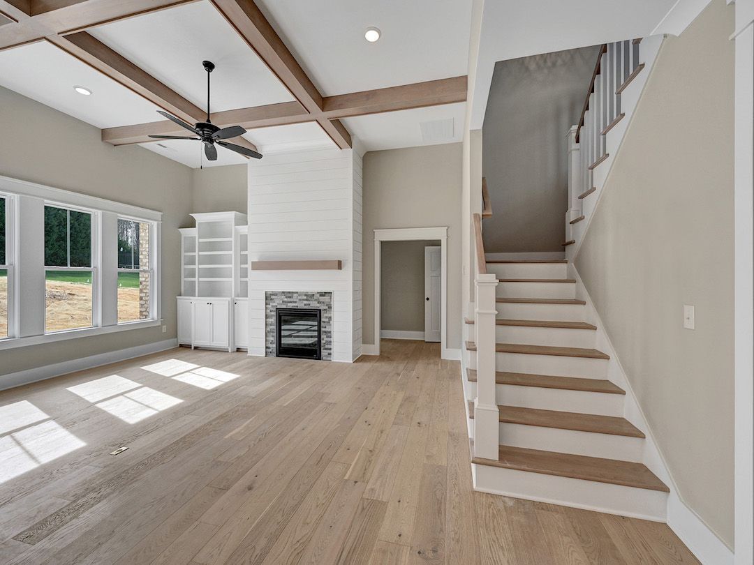 A living room with hardwood floors , a fireplace , stairs and a ceiling fan.