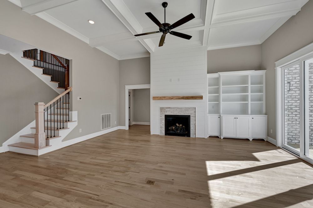 A living room with hardwood floors , a fireplace , stairs and a ceiling fan.