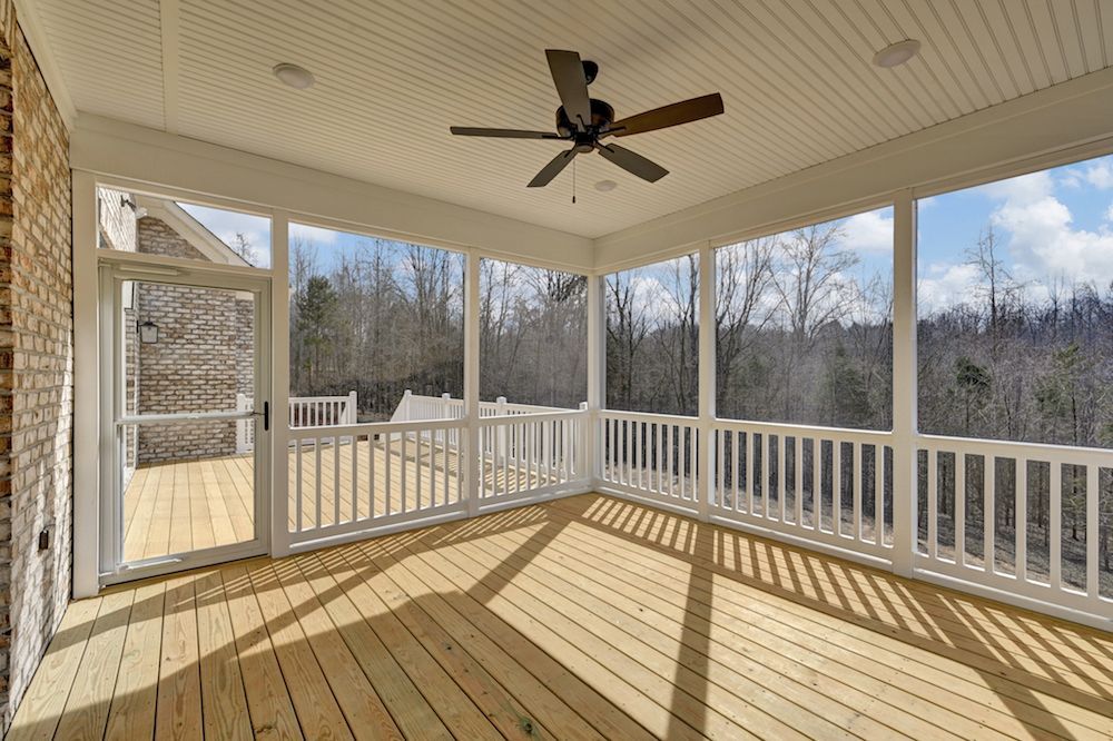 A screened in porch with a ceiling fan and a wooden deck.
