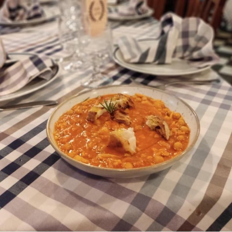 Una ciotola di stufato di ceci guarnita con pezzi di pane tostato e un rametto di rosmarino su una tovaglia a quadri.