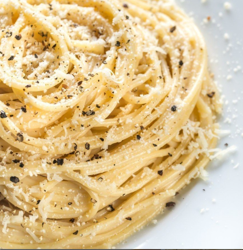 Primo piano di un piatto di spaghetti cacio e pepe, guarnito con formaggio grattugiato fresco e pepe nero macinato.