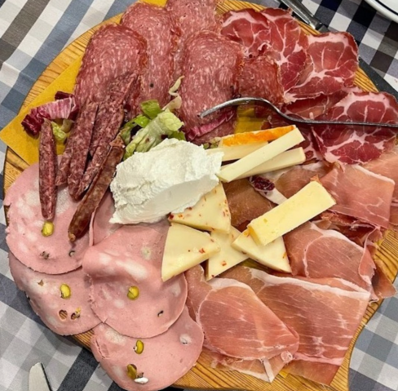 Un vassoio di legno con un assortimento di salumi, tra cui salame, mortadella, prosciutto crudo, affettati e formaggi.