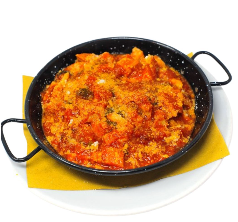 Una piccola padella nera contenente un piatto caldo a base di uova e pomodoro, servito su un tovagliolo giallo sopra un piatto bianco.