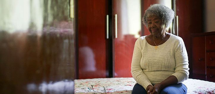 Elderly Black woman sitting on a floral bedspread