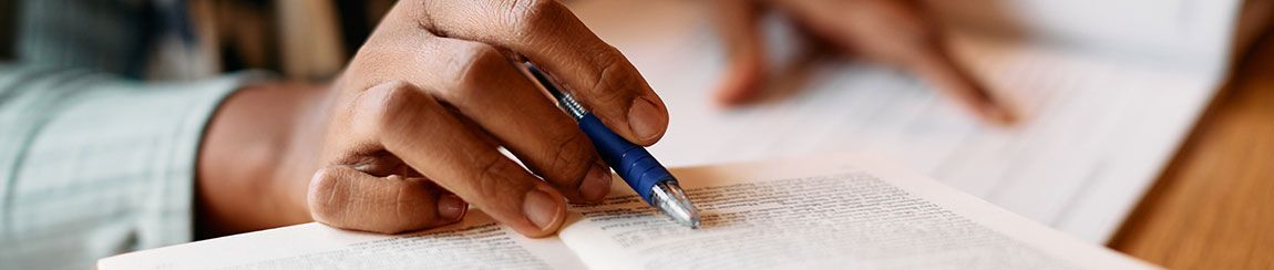 Close-up of an African American person’s hands writing their obituary in a notebook with a blue pen