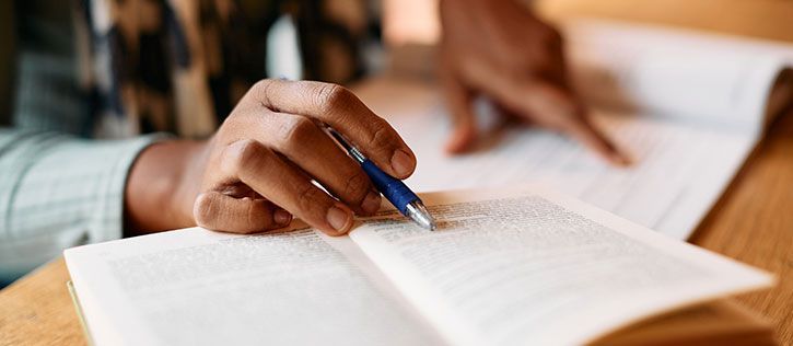 Close-up of an African American person’s hands writing their obituary in a notebook with a blue pen