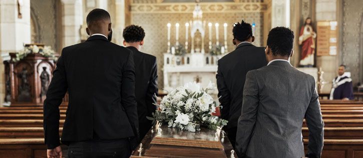 Four African American pallbearers carrying a casket down the aisle of a funeral chapel