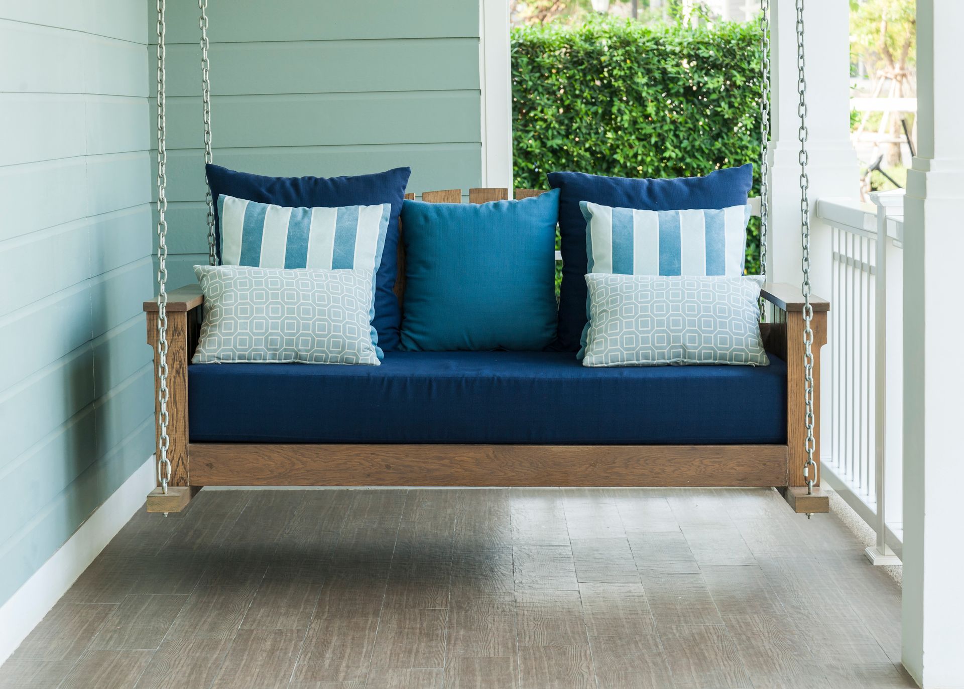 A porch swing with various custom outdoor pillows and cushions in shades of blue