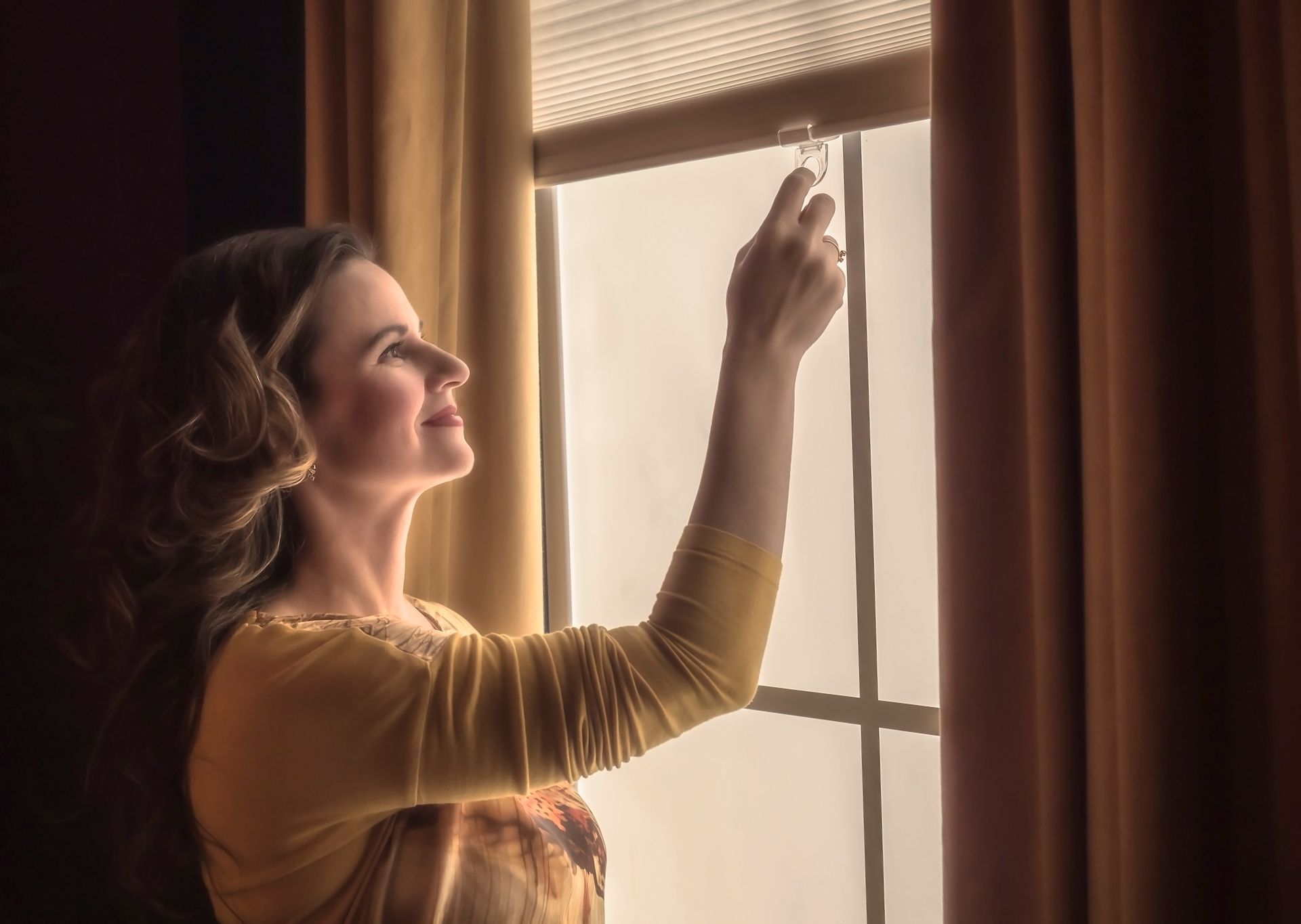 A woman opening her cordless window treatments paired with drapes to enjoy the outdoor view