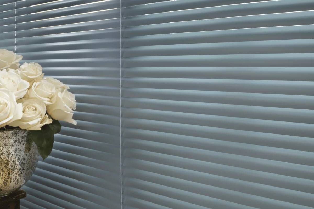 Hunter Douglas Modern Precious Metals® Mini Blinds on a Window Next to a Vase of White Roses