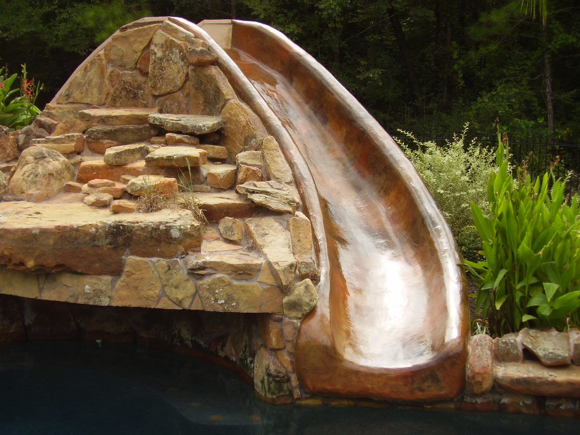 A large wooden slide is surrounded by rocks and plants
