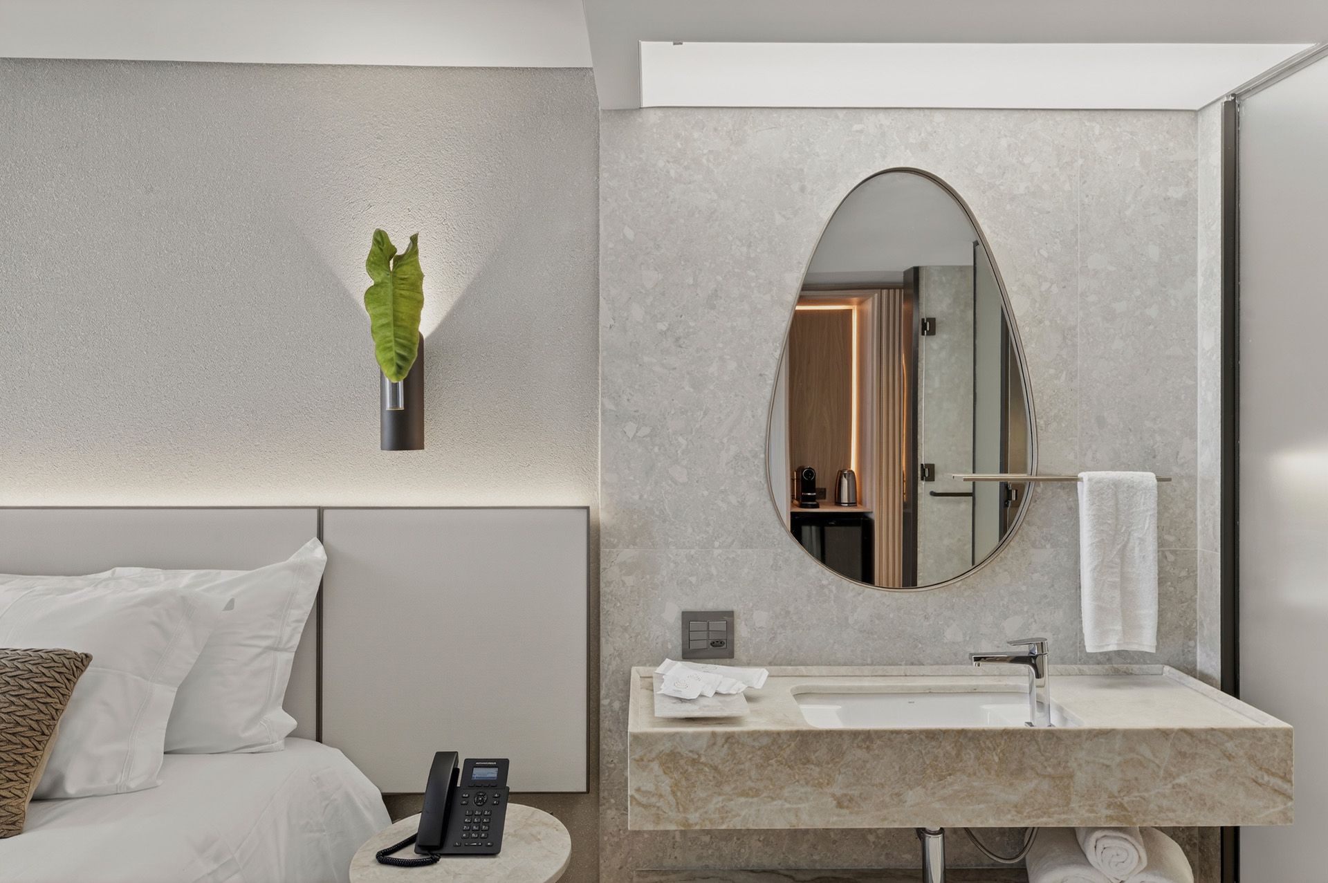 Quarto com cama, pia, espelho oval e planta fixada na parede.