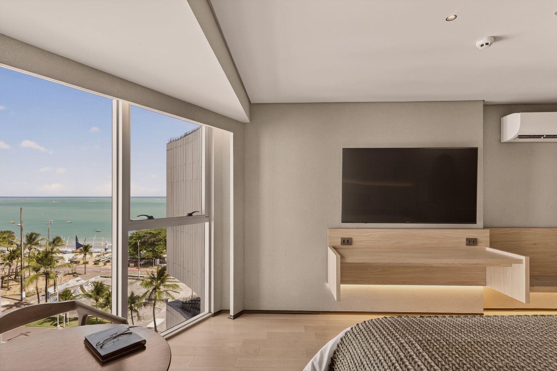 Quarto de hotel com vista para o mar, janela ampla, TV na parede e mobília moderna.