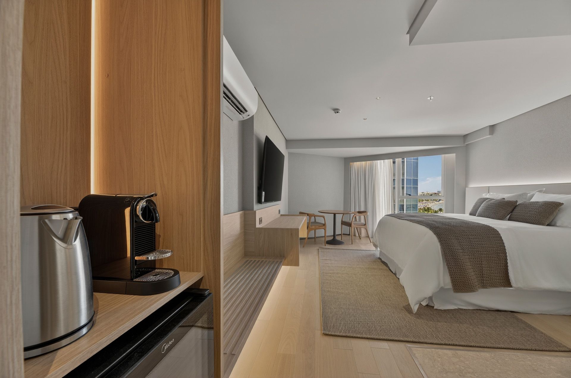 Quarto de hotel com cama, cafeteira e uma pequena mesa junto à janela.