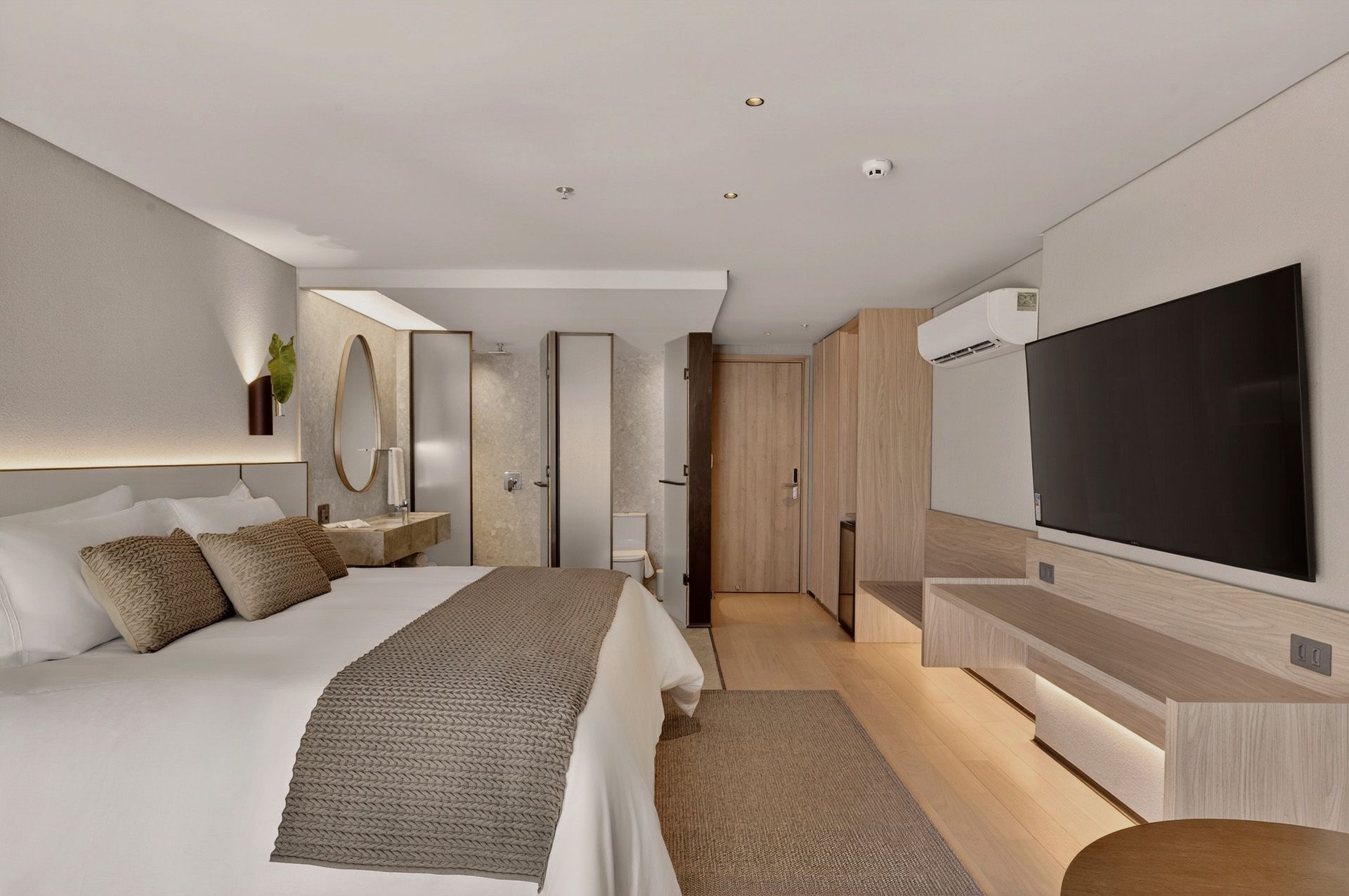 Quarto de hotel com cama grande, TV e acesso ao banheiro. Cores neutras e design moderno.