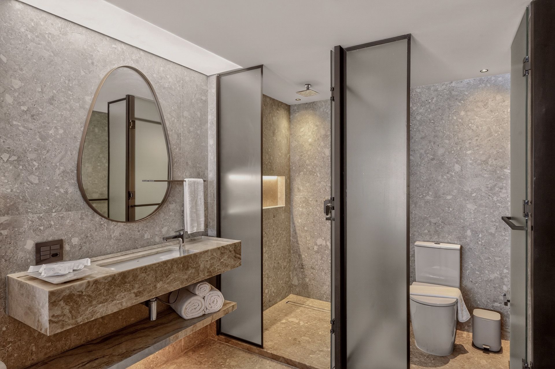 Banheiro moderno com paredes de pedra cinza, pia, espelho e porta de vidro fosco no box.