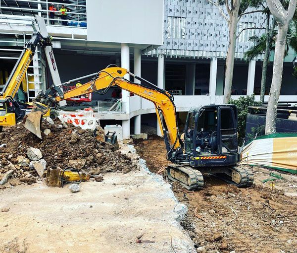 A yellow excavator is moving dirt in front of a building.