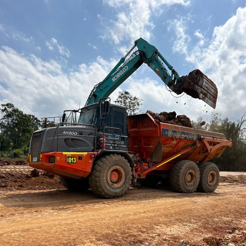 A dump truck is being loaded with dirt by a crane.