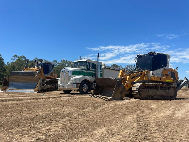 Two bulldozers and a truck are parked in a dirt field.