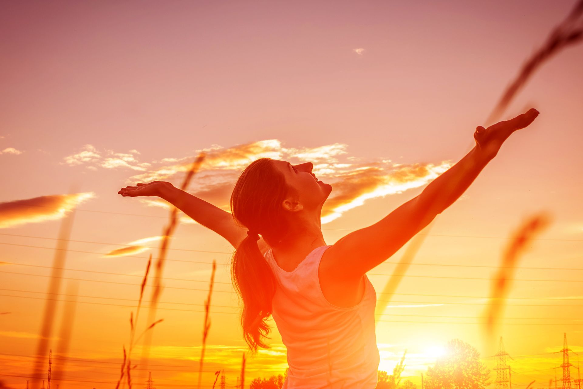 A woman is standing in a field with her arms outstretched at sunset.