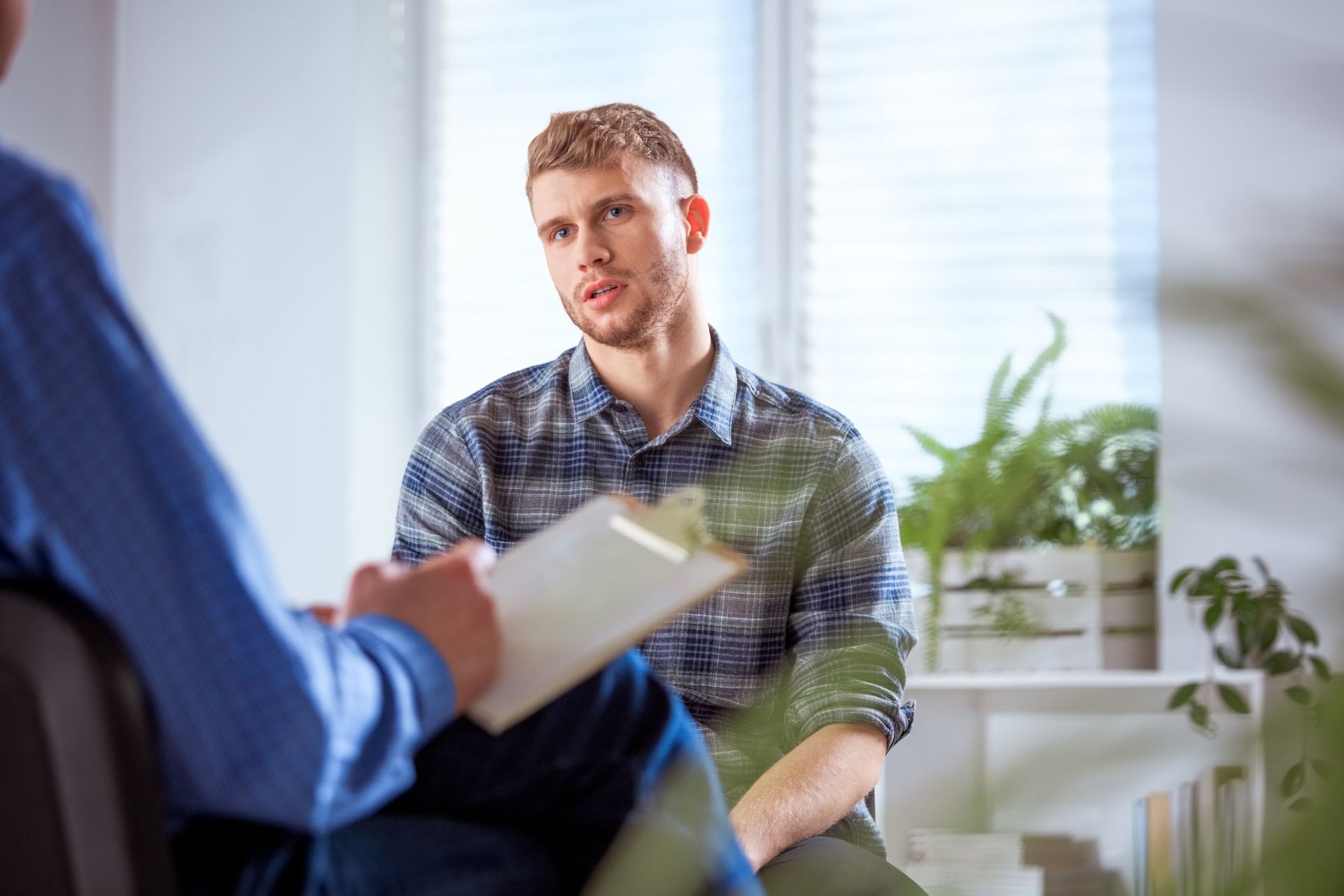 A man is sitting in a chair talking to a man holding a clipboard.