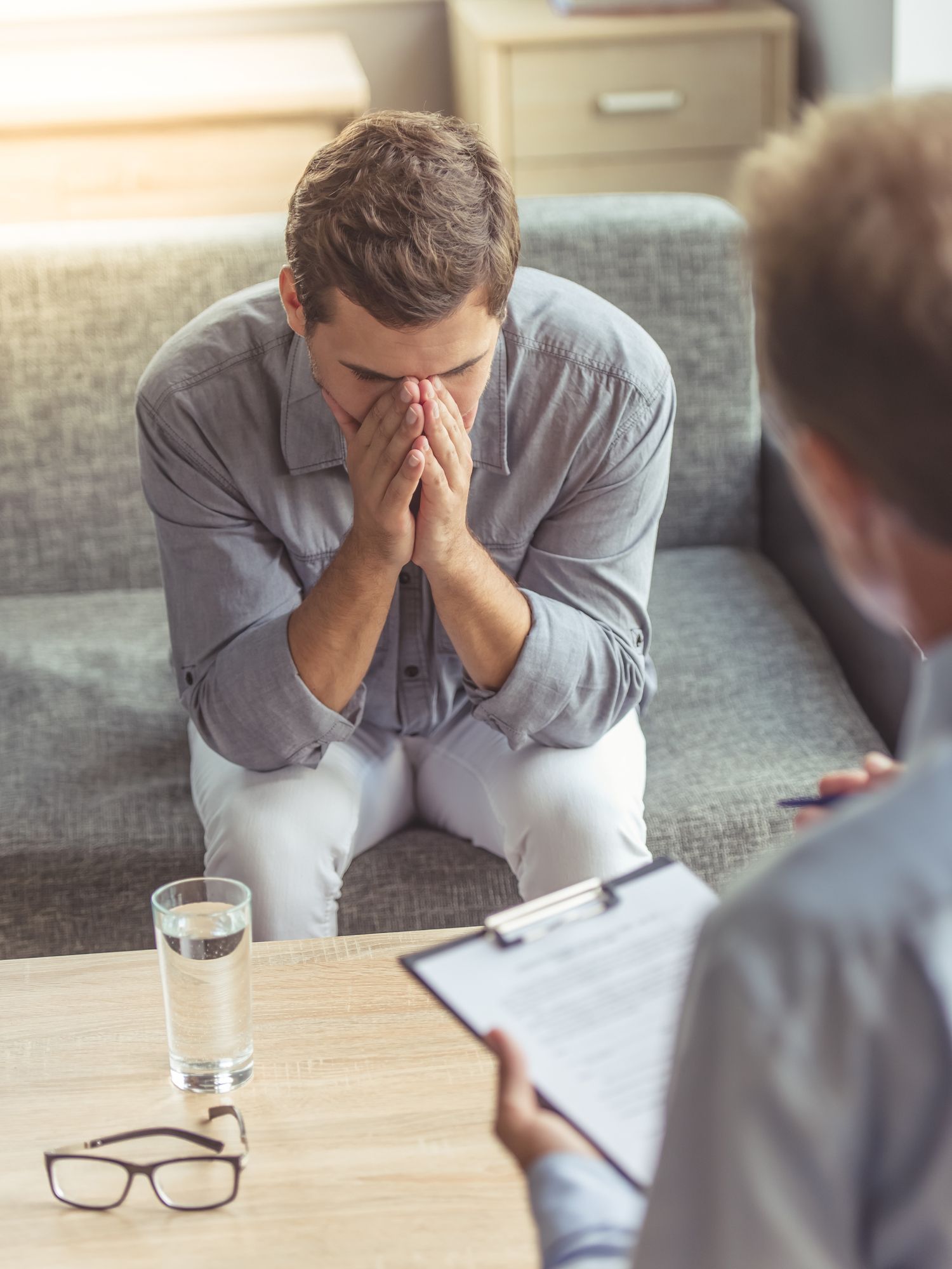A man is sitting on a couch covering his face while talking to a psychologist.