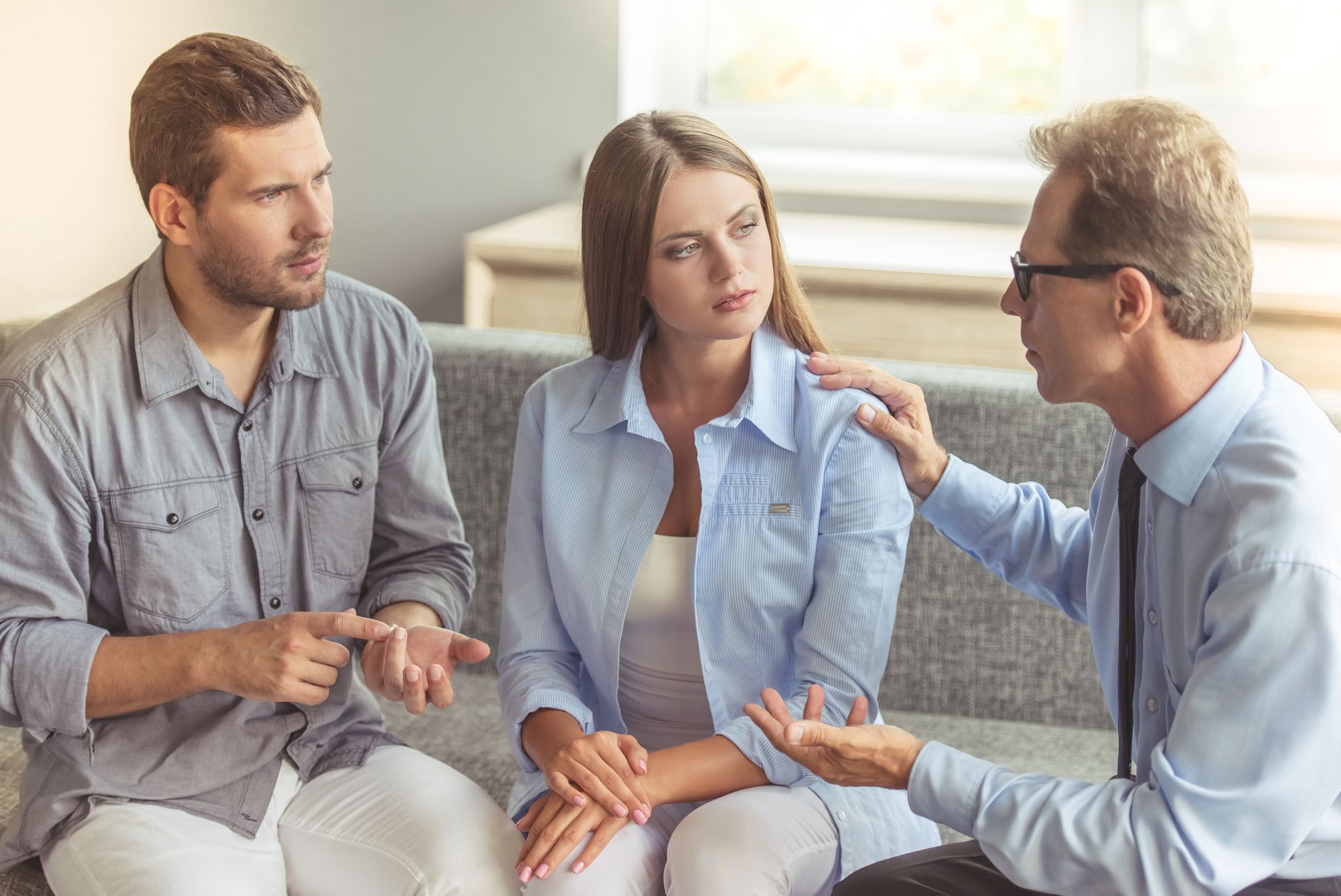 A man and a woman are sitting on a couch talking to a man.