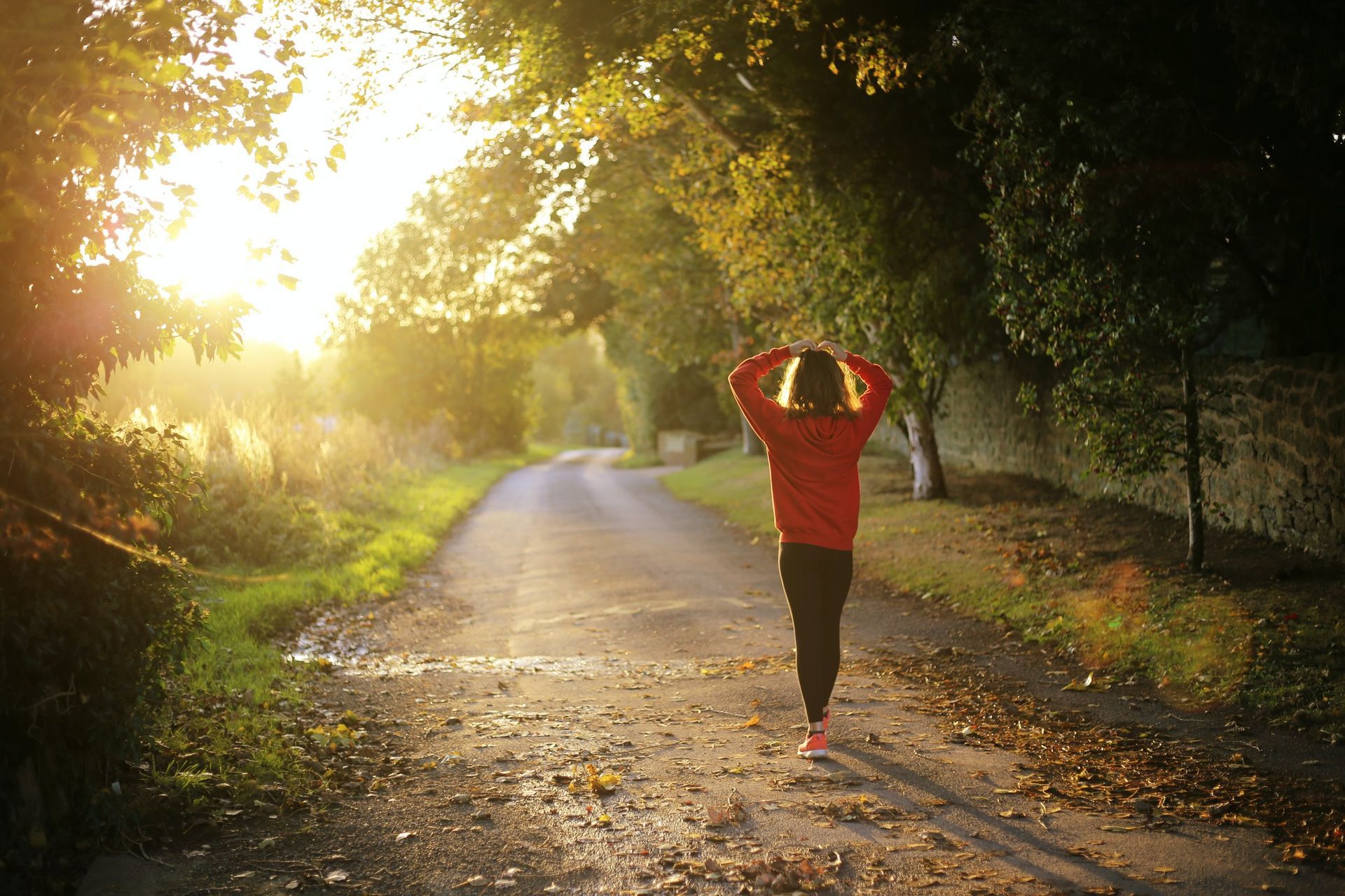A woman is walking down a dirt road at sunset.
