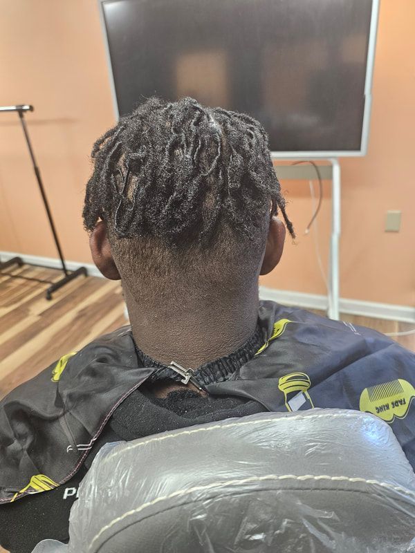 A man with dreadlocks is getting his hair cut in a salon.