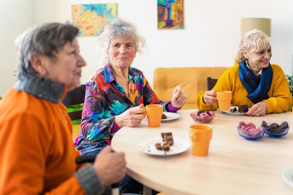 A group of elderly women are sitting around a table eating food and drinking coffee.