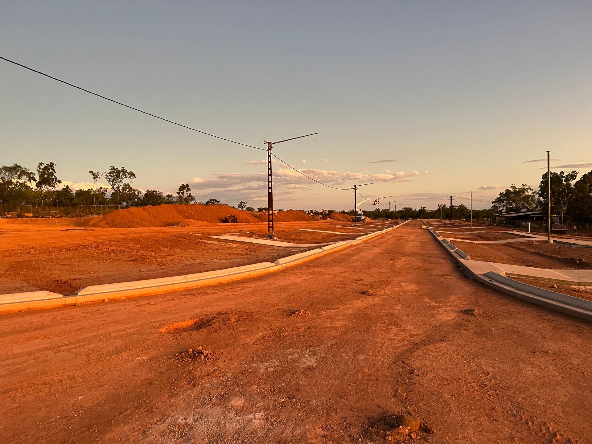 Empty paved road at sunset with streetlights and orange soil on both sides