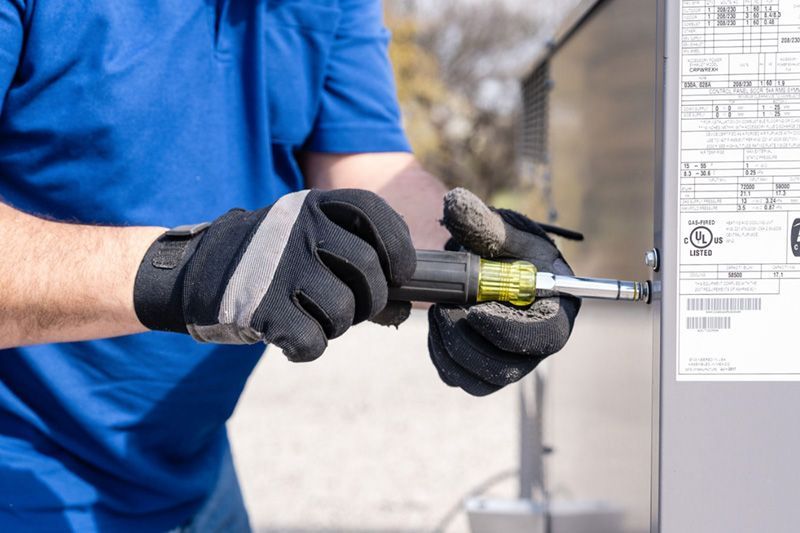 A man wearing gloves is using a screwdriver to fix a electrical box.