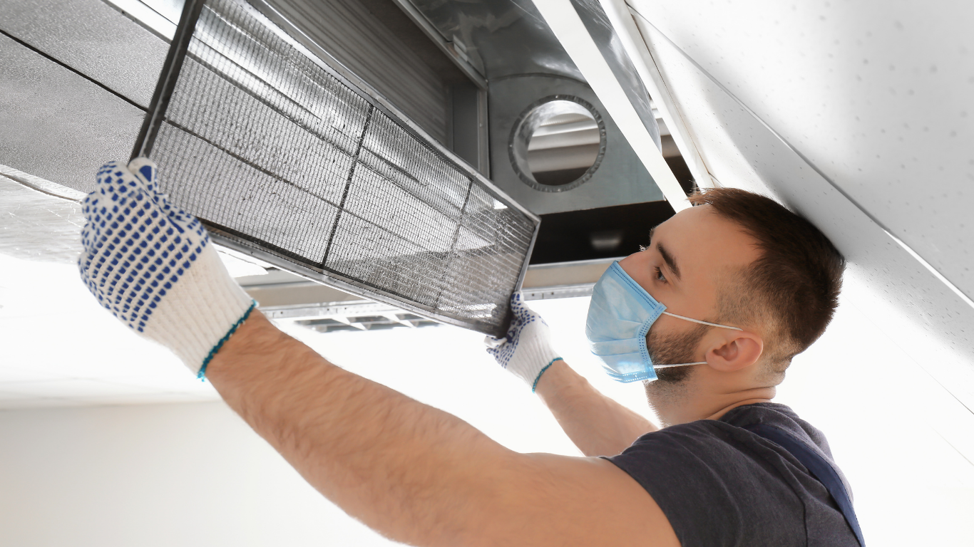 A man wearing a mask and gloves is cleaning an air conditioner.