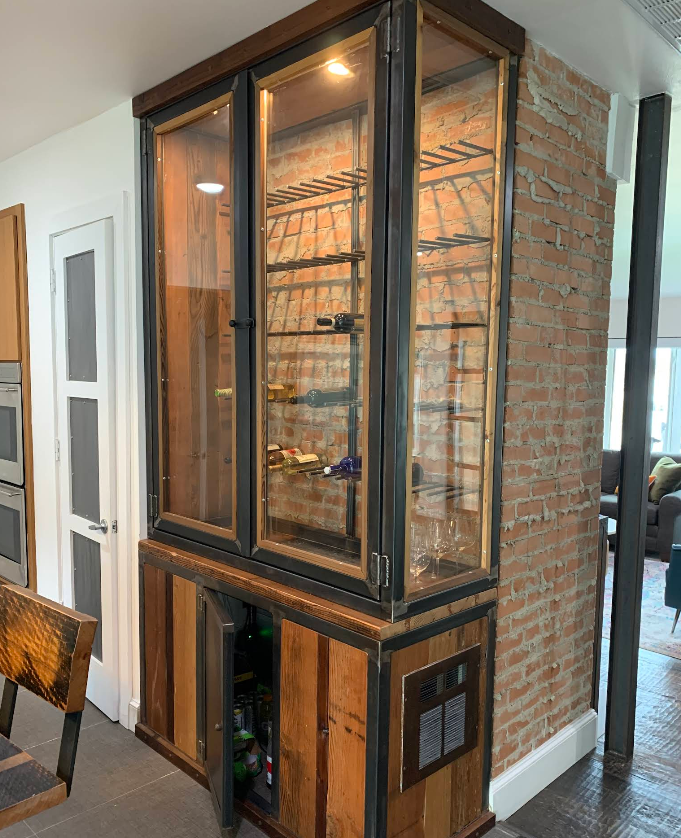A large wooden cabinet with glass doors is sitting next to a brick wall in a kitchen.