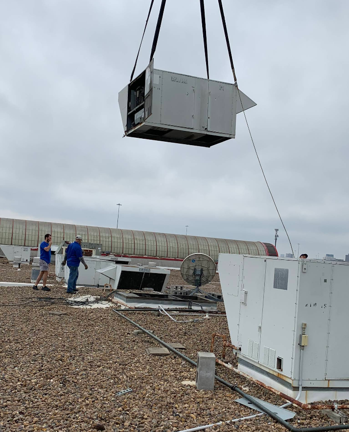 A large air conditioner is being lifted by a crane on top of a building.