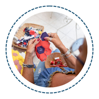 Mani di donna che cuciono una forma di fiore, circondate da stoffa e materiali per cucire.