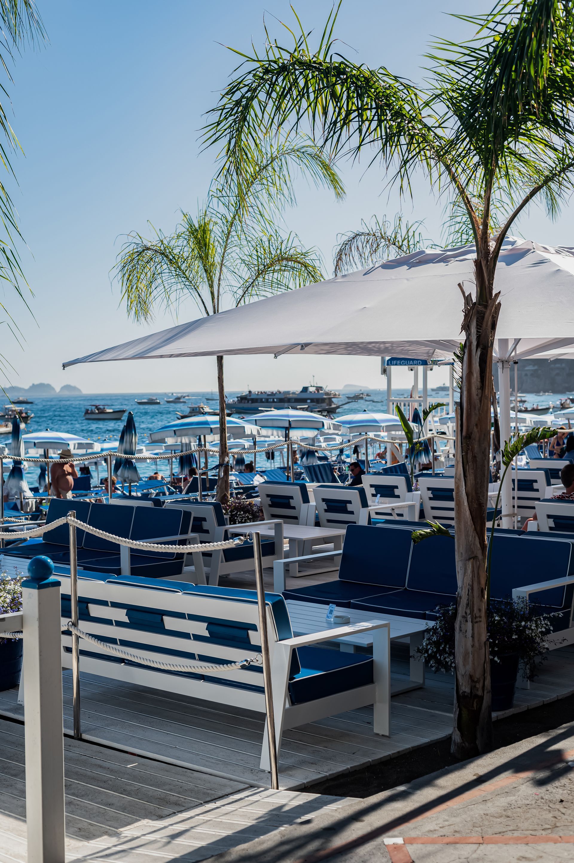 A beach restaurant with tables and chairs and umbrellas overlooking the ocean.
