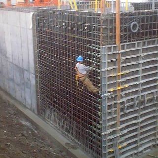 A construction worker is climbing up a concrete wall.